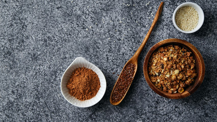 Healthy sweets cooking ingredients: granola, sesame and flax seeds, cocoa in separate bowls on gray background. Flatlay with copy space