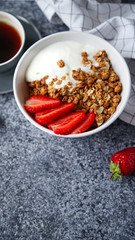 Perfect breakfast: crunchy granola with yoghurt and strawberries with a cup of black coffee on gray bakcground. Flat lay with copy space