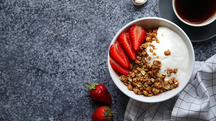 Perfect breakfast: crunchy granola with yoghurt and strawberries with a cup of black coffee on gray bakcground. Flat lay with copy space