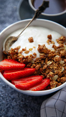 Close up shot of perfect breakfast: crunchy granola with yoghurt and strawberries with a cup of black coffee on gray bakcground.
