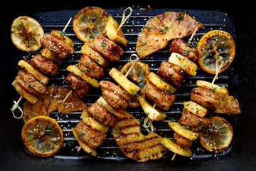 Photo sur Plexiglas Grill / Barbecue Brochettes grillées avec boulettes de poulet et ananas aux herbes sur une plaque de grill. Brochettes de fruits et de viande