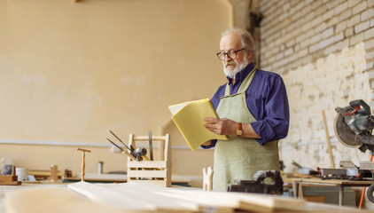 side view image of serious old smart carpenter drawing graph in the exercise book. write ideas. copy space