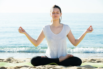 Fototapeta na wymiar Female 20-30 years old in white T-shirt is sitting and practicing meditation