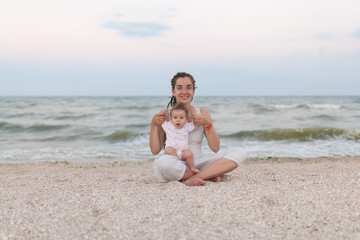 Fototapeta na wymiar Happy family mother and child daughter doing yoga, meditate in lotus position on beach at sunset