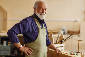 joyful old builder wearing apron and blue shirt is having rest at workplace