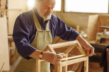 concept of diy. old man is making a sketch of birds house from wood