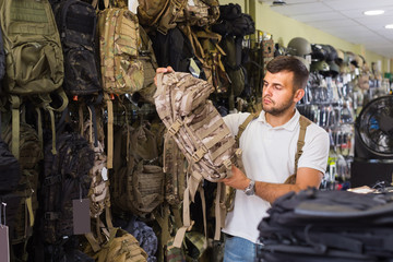 Man choosing textile backpack gun in military shop