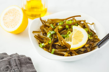 Sea kale kelp salad with oil and lemon in a white plate, white background.