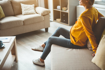 Relaxed expectant mother is sitting on comfortable sofa in living room 