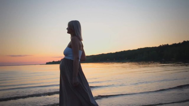 Beautiful silhouette pregnant girl at sunset goes on beach