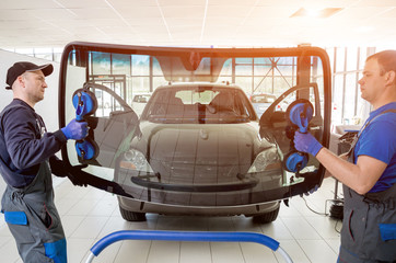 Automobile special workers replacing windscreen or windshield of a car in auto service station...