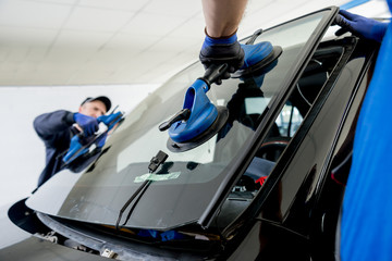 Automobile special workers replacing windscreen or windshield of a car in auto service station...