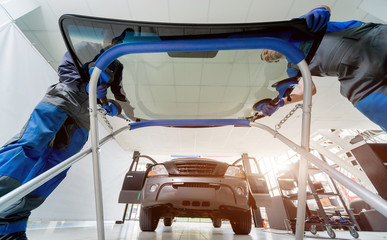 Automobile special workers replacing windscreen or windshield of a car in auto service station...