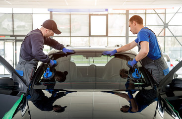 Automobile special workers replacing windscreen or windshield of a car in auto service station...