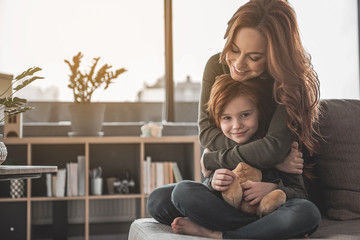 Perfect day together. Portrait of caring mother hugging her daughter at home. They are showing...