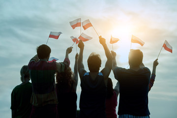 Poland patriotic people with small flags, back view. Blue morning sky background.