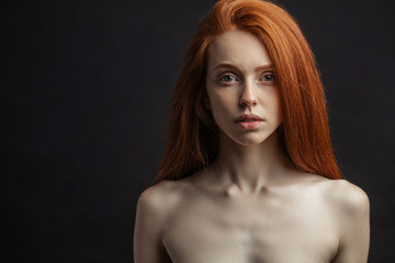 Amazing young girl with long gorgeous red hair and strapless bra on black background with copyspace...