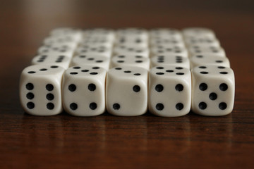 Dice in random order lie close to each other on a dark table. A lot of cubes are made in the form of a square of twenty-five pieces. Background and edges in the blur.