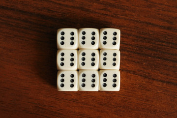 Many dice are lying close to each other on a dark table. Cubes form a square of nine pieces. Background in blur.