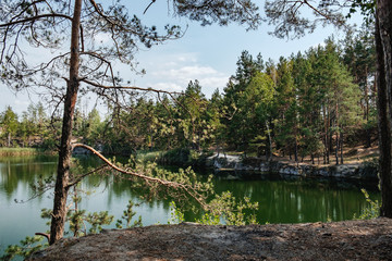Picturesque landscape with a lake in the middle of a coniferous forest in Korostyshiv quarry, Zhytomyr district, northern Ukraine. Branches of pine overhanging lake in the foreground