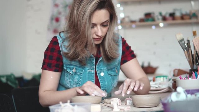 attractive young Caucasian woman spends time behind a creative hobby. the girl enthusiastically sculpts a plate of clay in the workshop