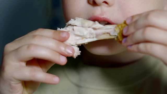 Close up shot of a young girl taking a bite of chicken nugget indoor.