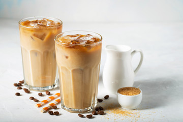 Ice coffee in a tall glass with cream poured over and coffee beans. Cold summer drink on a light blue background