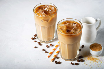 Ice coffee in a tall glass with cream poured over and coffee beans. Cold summer drink on a light blue background