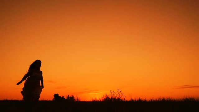 Silhouette of young girl jumping against orange sky