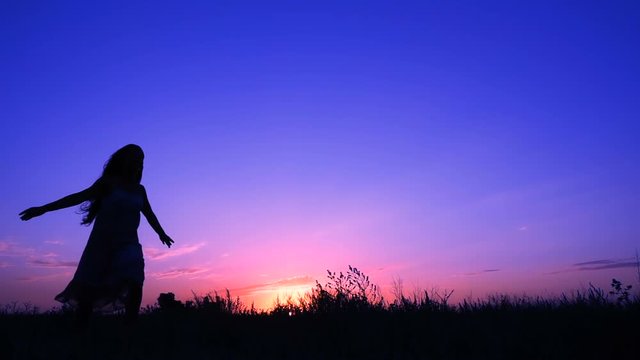 Silhouette of young girl running against pink sky