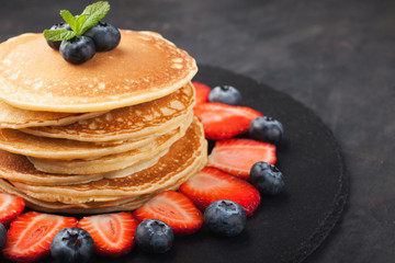 Delicious pancakes close up, with fresh blueberries, strawberries on a black stone background