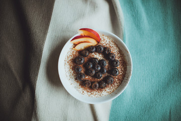 useful nutritious tasty breakfast tiramisu dessert and fresh blueberries berries and peach in a round white bowl on a plaid, flatlay
