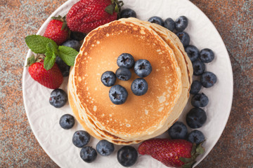 Close-up delicious pancakes, with fresh blueberries, strawberries and maple syrup on a rusty background