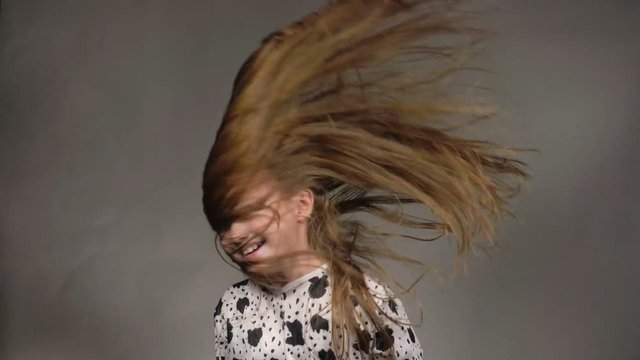 Happy little girl in the studio on a gray background. She jumps, shows different emotions. Hair fluttering from the wind. Super slow motion, shot at 180fps.