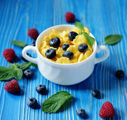 Healthy eating, food and diet concept - Cornflakes with berries raspberries and blueberries on blue wooden background.
