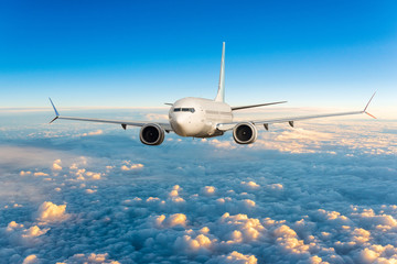 Fototapeta na wymiar Front view of aircraft in flight. The passenger plane flies high above the clouds and blue sky. Business travel and summer trip concept