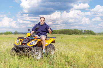 Naklejka na ściany i meble Man riding ATV quad bike at beautiful nature countryside. Driver showing thumbs up sign. Scenic meadows and fields landscape. Travel and adventure concep
