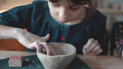 child is making a plate of clay. a lesson in pottery. little girl makes patterns on a clay stamp