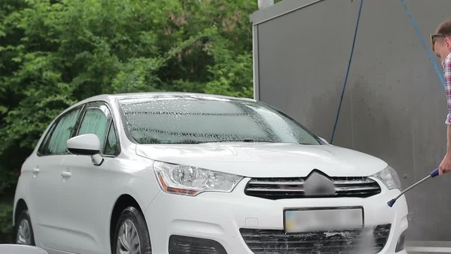 A young man washes his white car