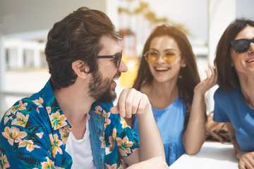 Side view profile of happy young man talking with girls and laughing. They are relaxing at the summer beach 