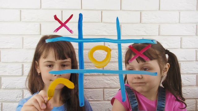 Tic-tac-toe. Children draw with colors. Sisters play together.