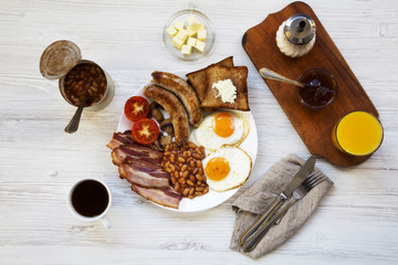 Full english breakfast with fried eggs, bacon, sausages, beans and toasts on white wooden background, top view. Flat lay. From above.