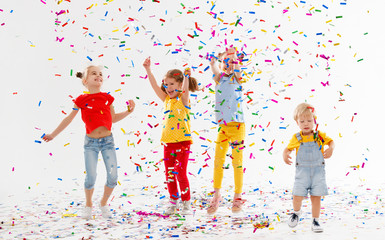 happy children on holidays  jumping in multicolored confetti on white