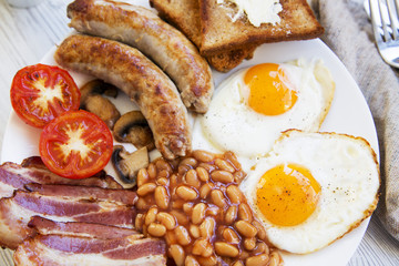 English breakfast with fried eggs, bacon, sausages, beans and toasts. Closeup.
