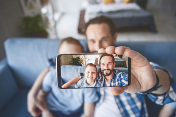 Portrait of outgoing parent and glad child doing photo by mobile