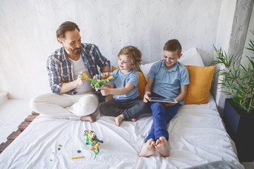 Full length portrait of happy parent having good time with satisfied children while situating in bedroom. Glad family concept
