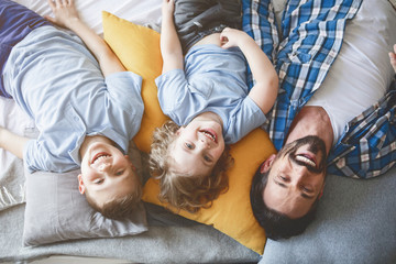 Top view portrait of satisfied sons relaxing on pillows near outgoing father. Happy family concept