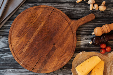top view of empty wooden cutting board, spices, cheese and vegetables on table