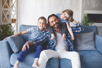 Portrait of outgoing dad and happy kids locating on cozy couch in living room. Positive family...