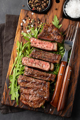 Closeup ready to eat steak new York beef breeds of black Angus with herbs, garlic and butter on a wooden Board. The finished dish for dinner on a dark stone background. Top view